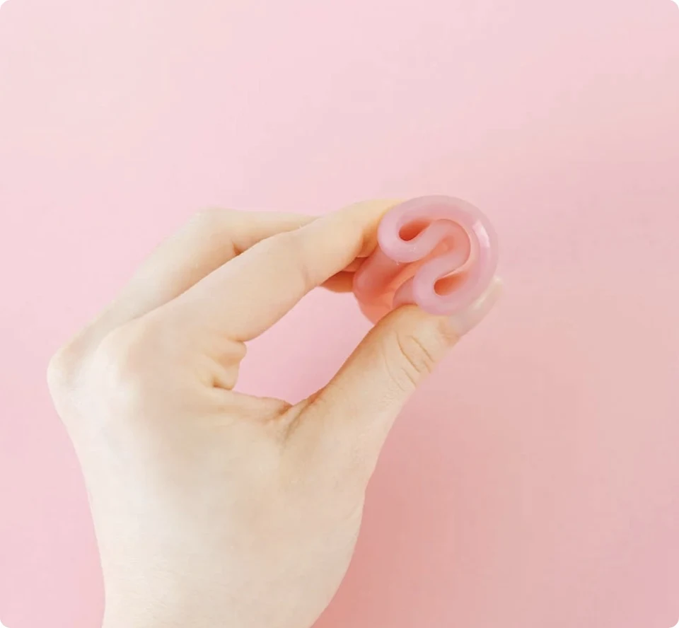 Folded pink Kallypso menstrual disc held between two fingers